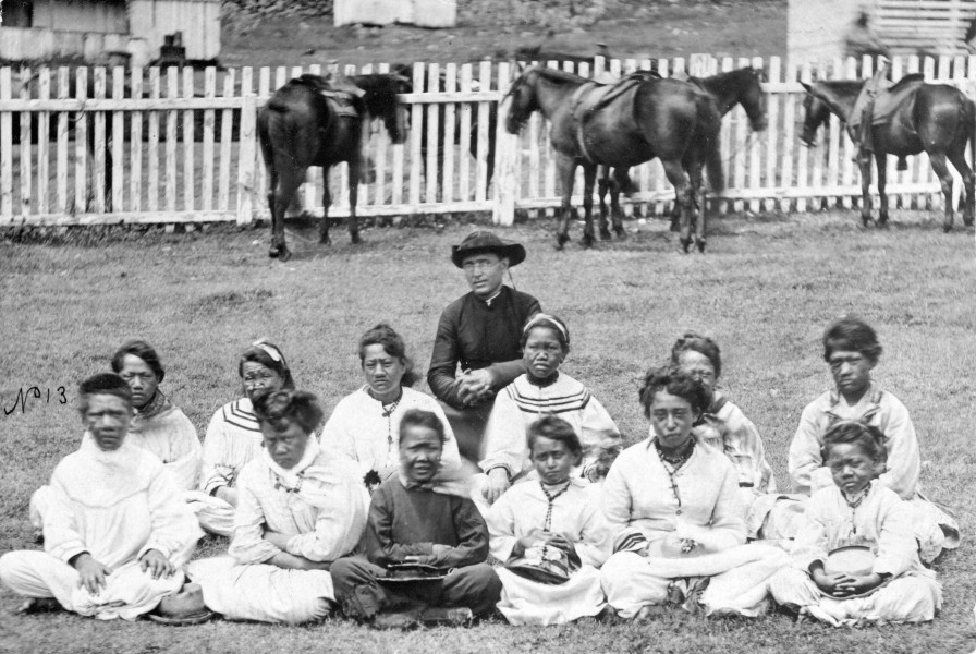 Henry L. Chase [Public domain], <a href="https://commons.wikimedia.org/wiki/File:Father_Damien_with_the_Kalawao_Girls_Choir,_at_Kalaupapa,_Molokai,_circa_1878.jpg"  target="_blank">via Wikimedia Commons</a>